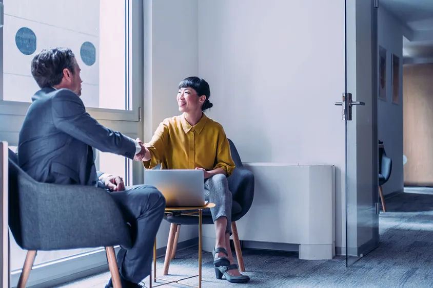 Two professionals meeting at a small table shaking hands