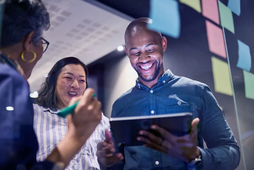 A tech team standing together over a tablet smiling