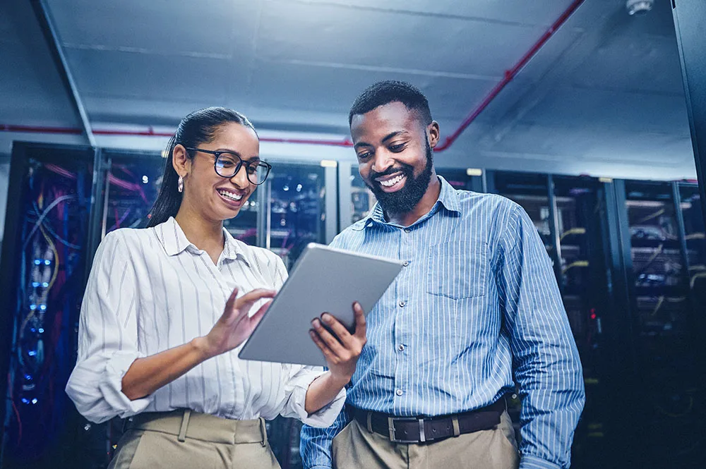 Two young members of a tech team smiling looking at a tablet