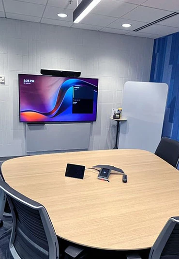 An empty conference room with a television, phone, and remote on a table
