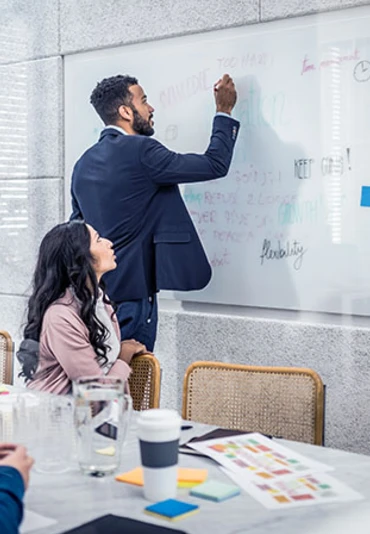 A young male team leader writing on a white board with a team