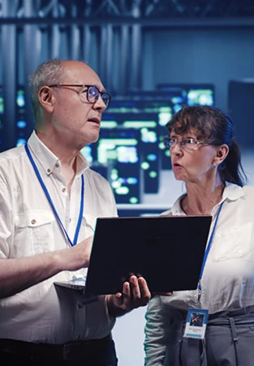 An older man and woman in a tech enivornment dicussing something on a laptop
