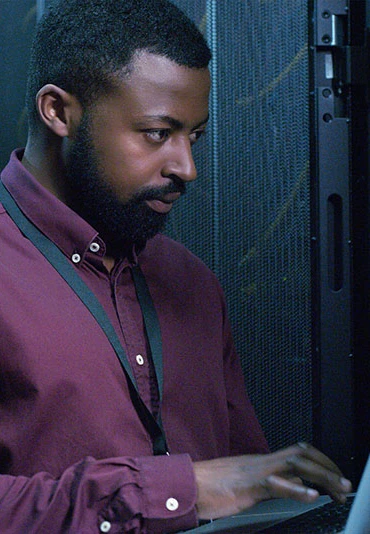 A man with a laptop standing in front of computer hardware conduction maintenance