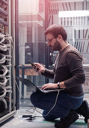 A male IT professional kneeling in front of network equipment